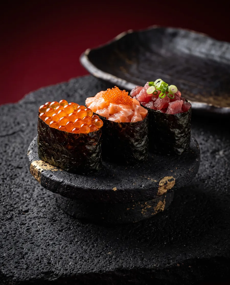 Três gunkans de ikura, salmão e atum num pedestal de pedra